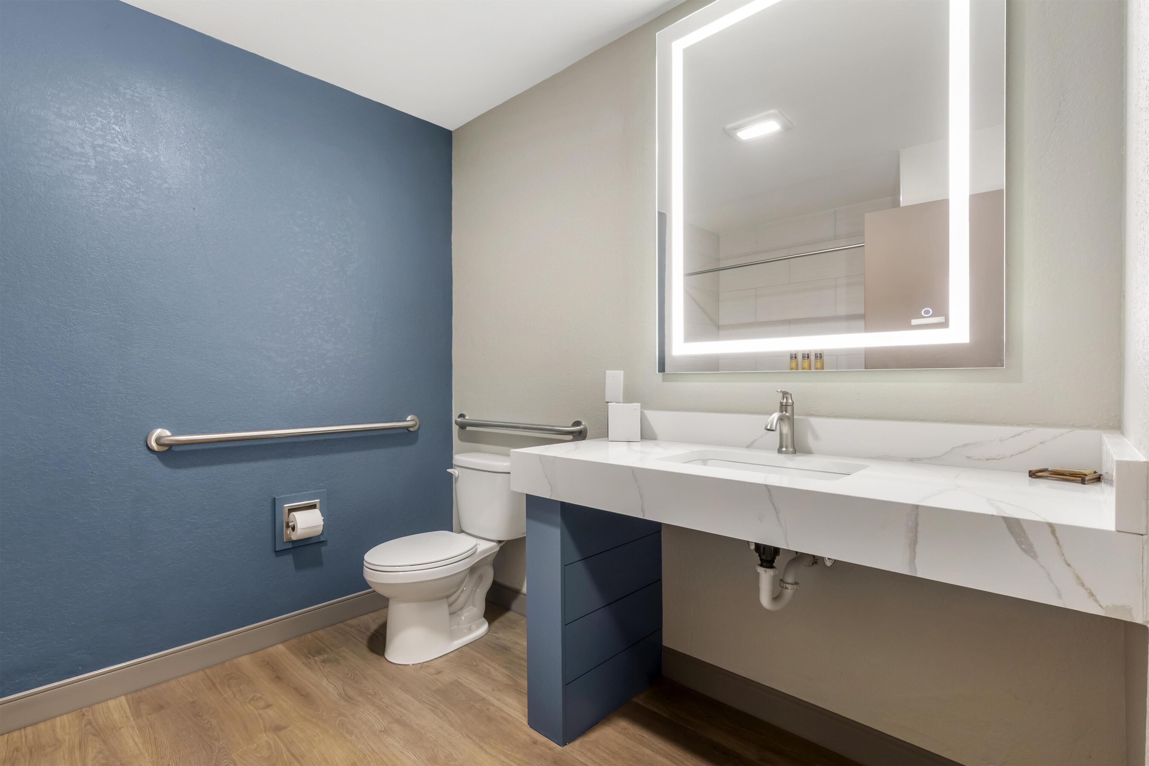 Un baño con pared azul, inodoro blanco, tocador con espejo y barandilla.