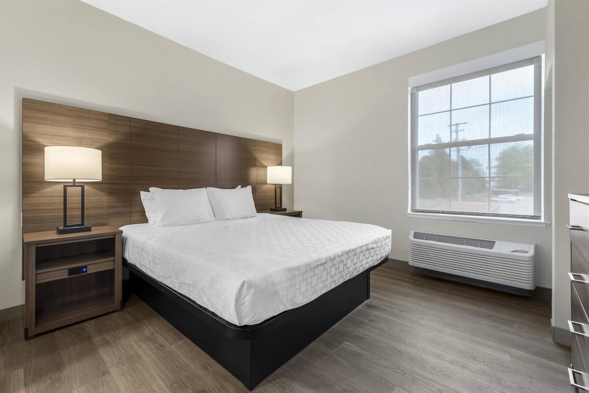 A modern hotel room with a large bed, bedside lamps, a built-in heater, and a large window.