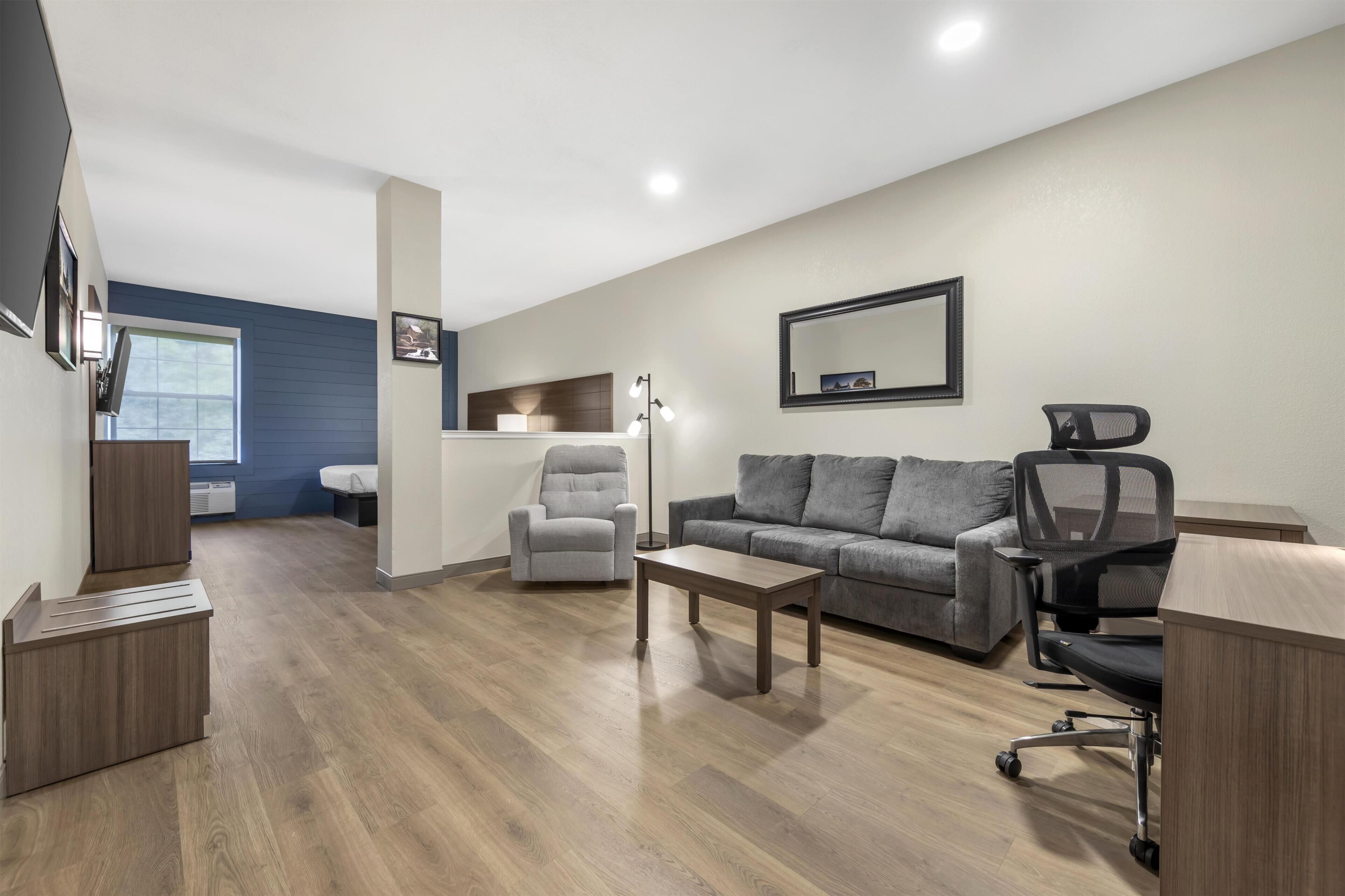 A modern living room with a grey sofa, a grey armchair, a wooden coffee table, a black office chair, and a desk.