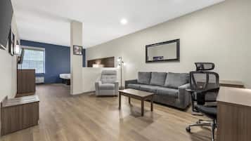 A modern living room with a grey sofa, a grey armchair, a wooden coffee table, a black office chair, and a desk.