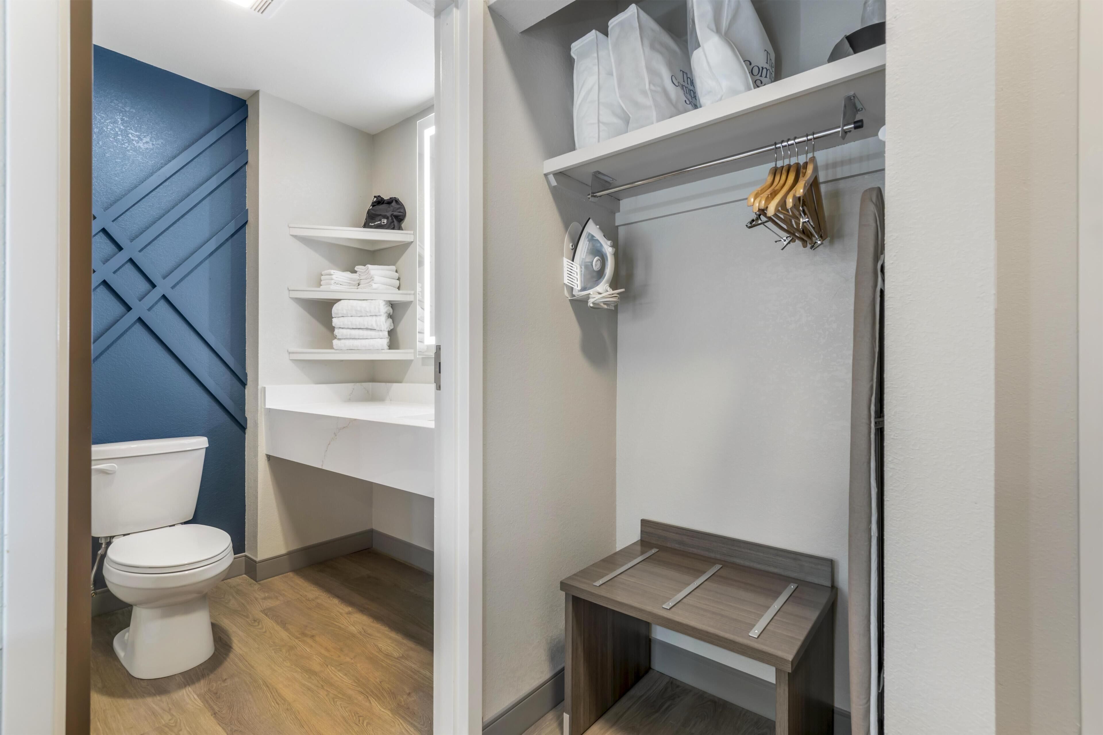 Une salle de bain moderne comprenant des toilettes, des étagères avec des serviettes, un espace douche et un petit banc en bois.