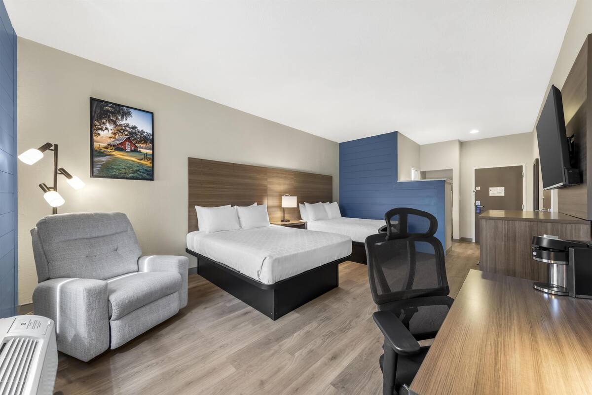 A hotel room with a bed, a desk, a chair, a TV, and a painting on the wall.