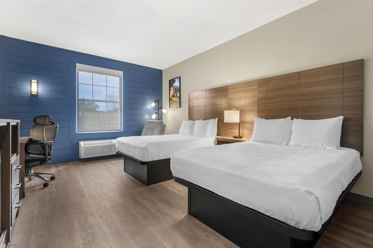A hotel room with two beds, a desk, and a chair.