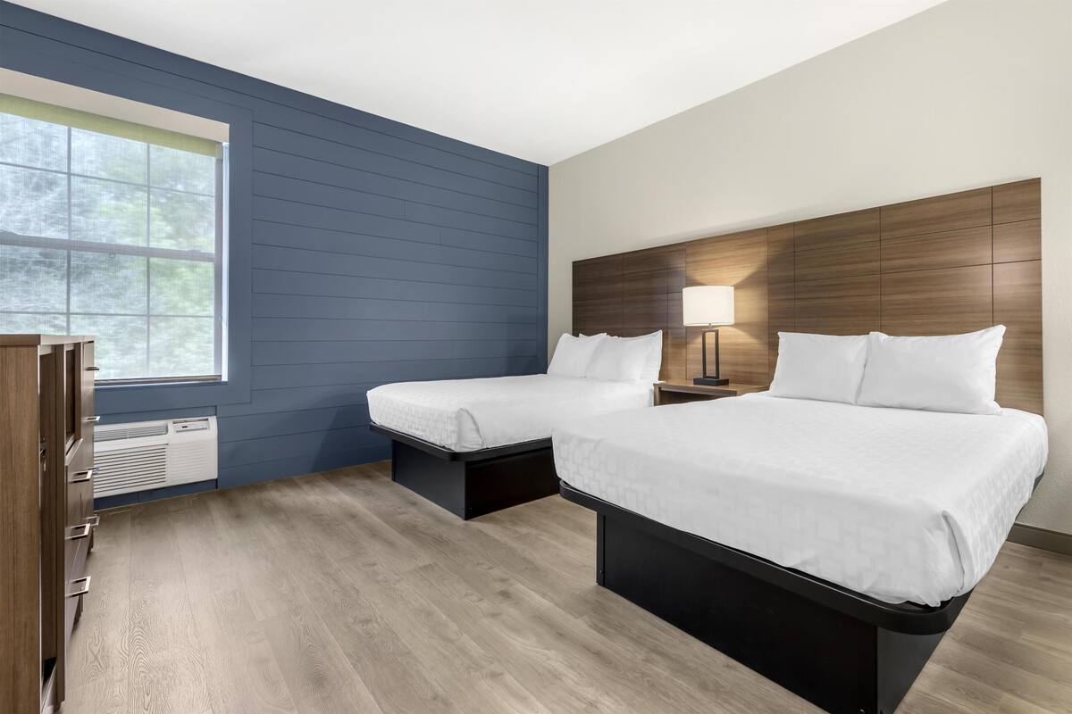 A hotel room with two beds, a desk, and a window.