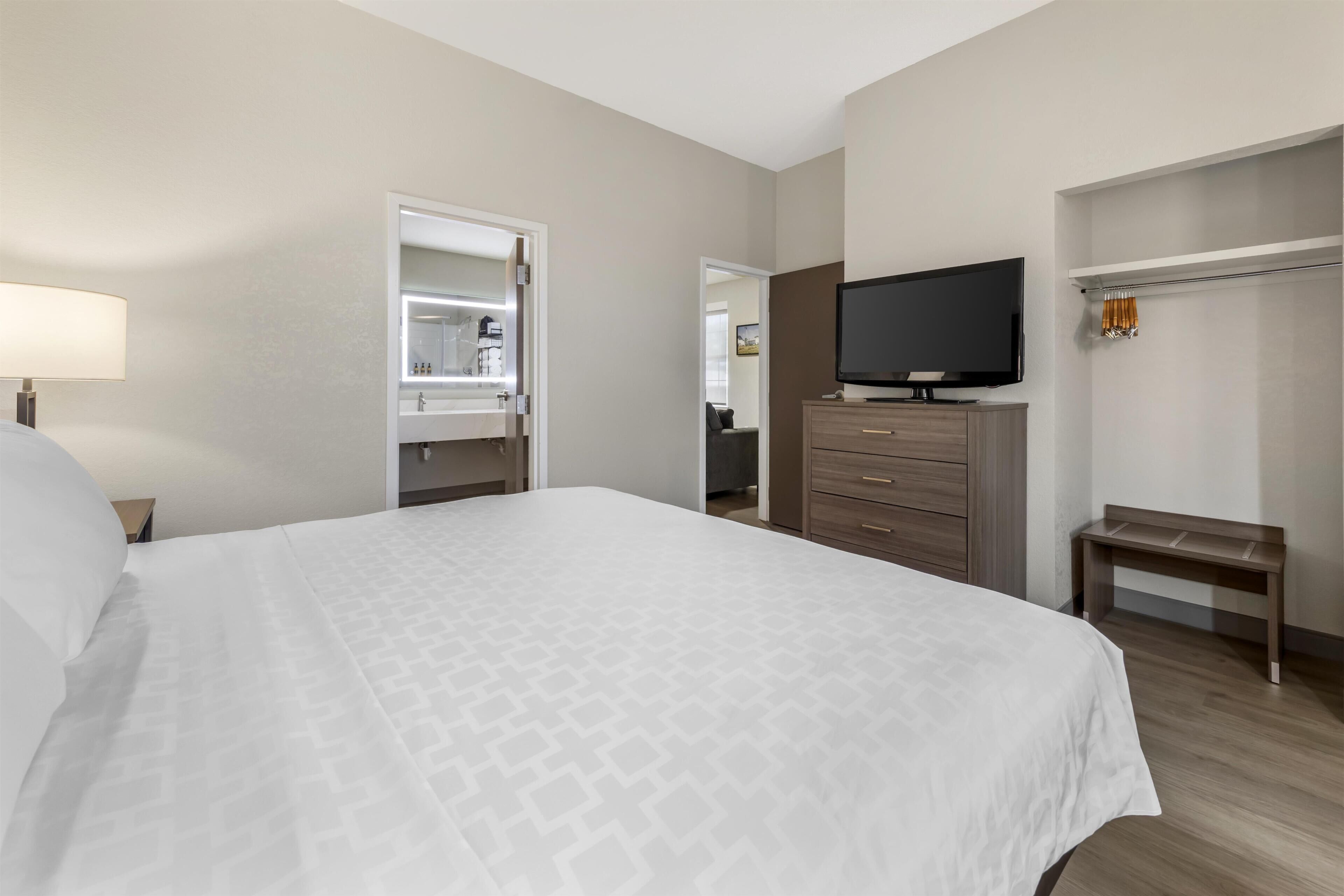 Una habitación de hotel con cama, televisor, armario y un banco.