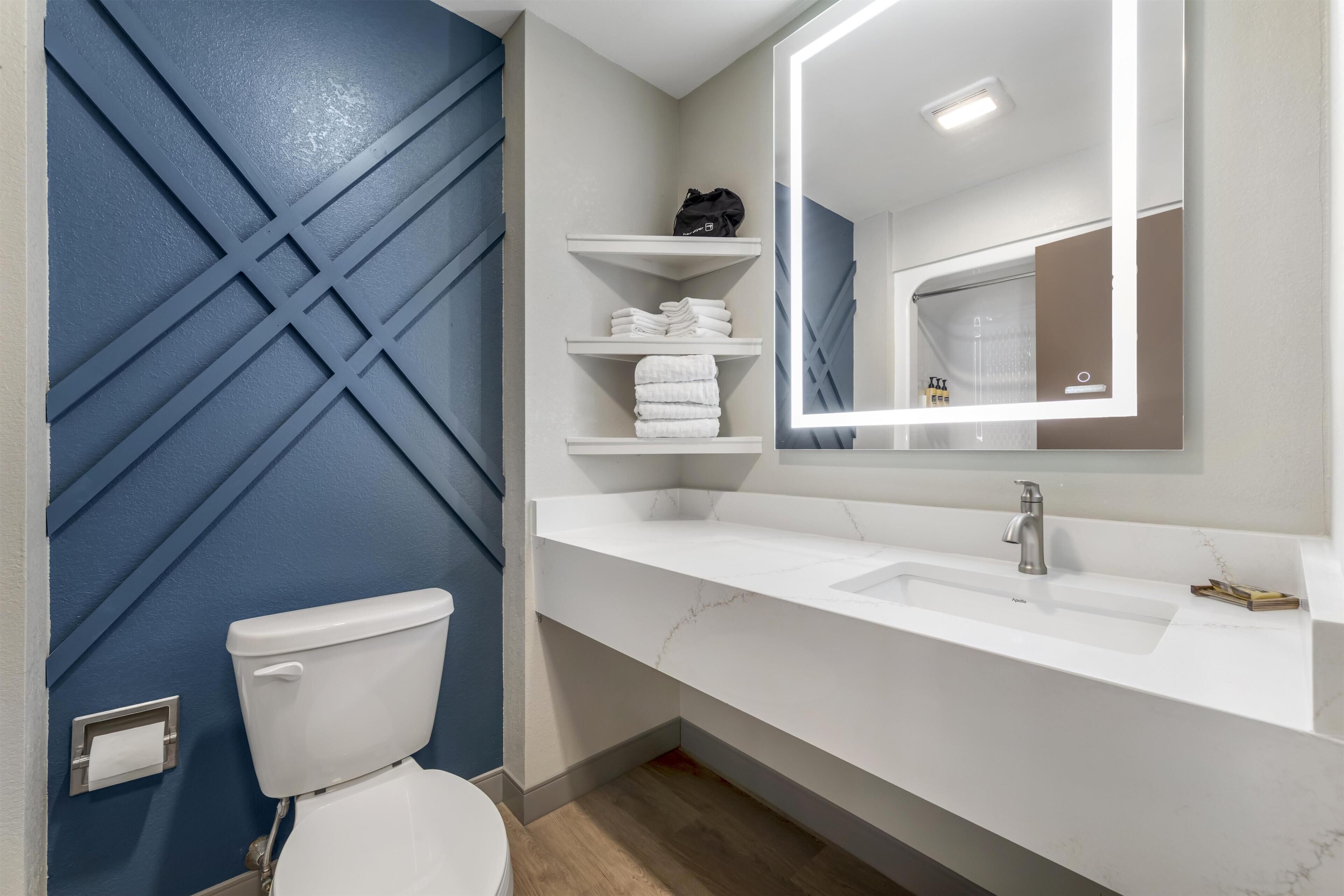 Ein Badezimmer mit Toilette, Waschbecken mit Marmorplatte und Regalen mit Handtüchern.
