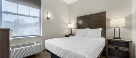 A hotel room with a bed, two bedside tables with lamps, a window, and a built-in heater.