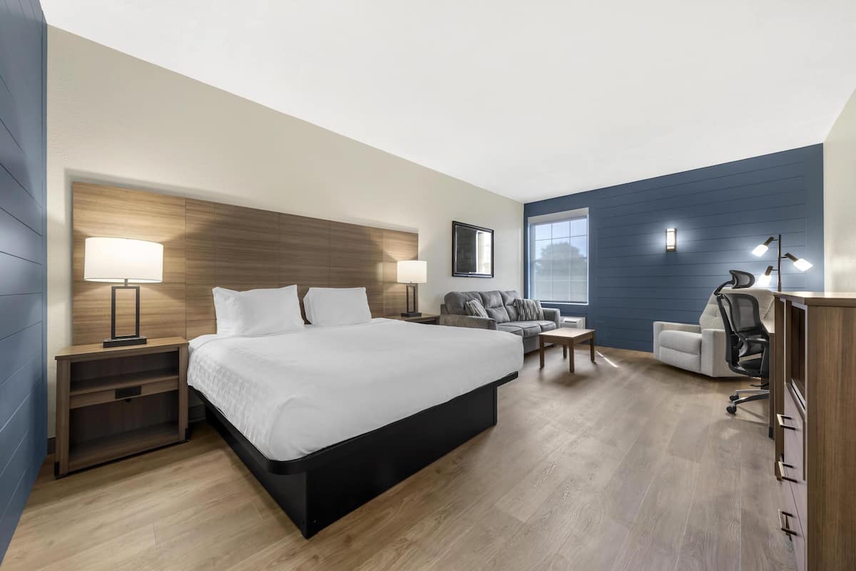 A modern hotel room with a large bed, a desk, a sofa, and a chair.