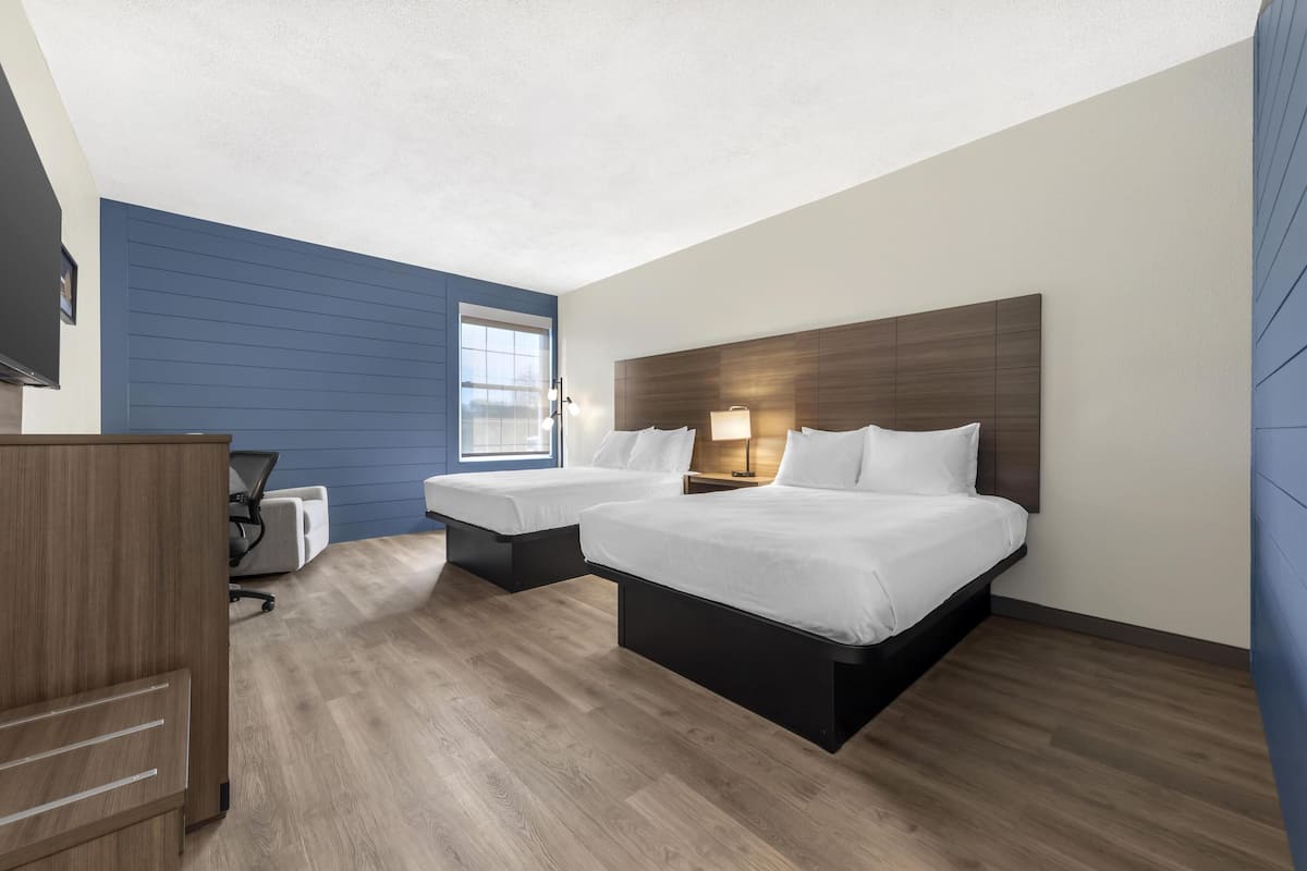 A hotel room with two beds, a desk, and a chair.