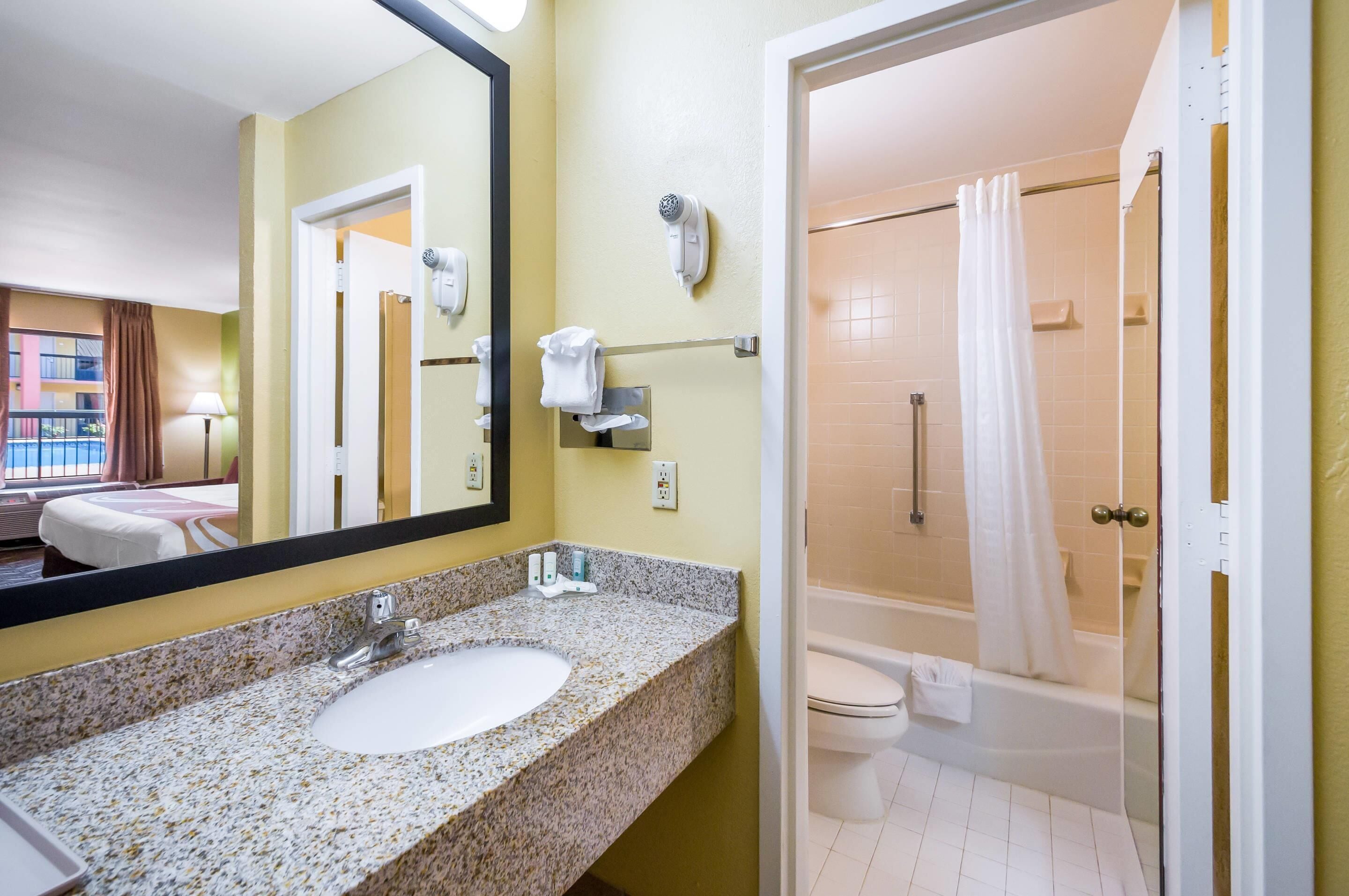 Une salle de bain d’hôtel équipée d’un lavabo en granit, d’un miroir, d’un sèche-cheveux et d’une douche avec rideau.