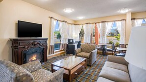 A hotel room with a fireplace, a flat-screen TV, a sofa, a coffee table, and a dining area with a table and chairs.