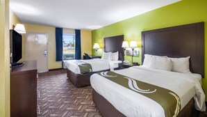 A hotel room with two beds, a desk, and a television.