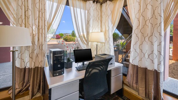 A hotel room with a desk, computer, and a view of the outdoors.