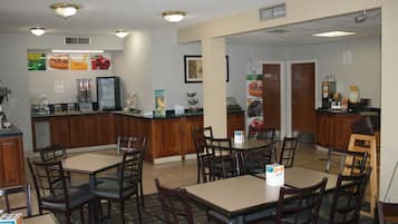 Zona de dinar d'hotel amb diverses taules i cadires, una barra de cuina i diferents distribuïdors d'aliments i begudes.