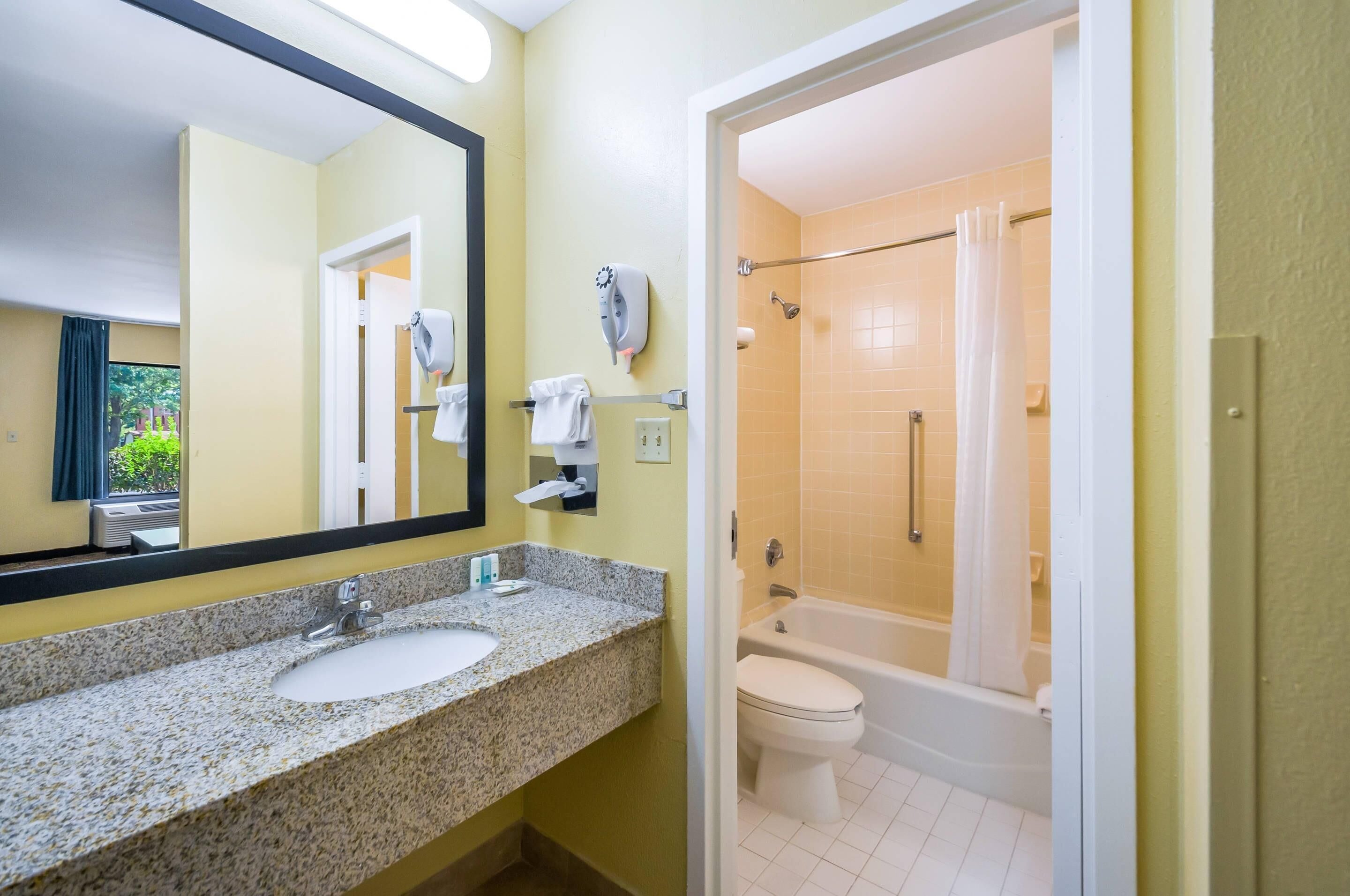 Baño con lavamanos de granito, espejo, toallero, secador de pelo y zona de ducha con bañera.