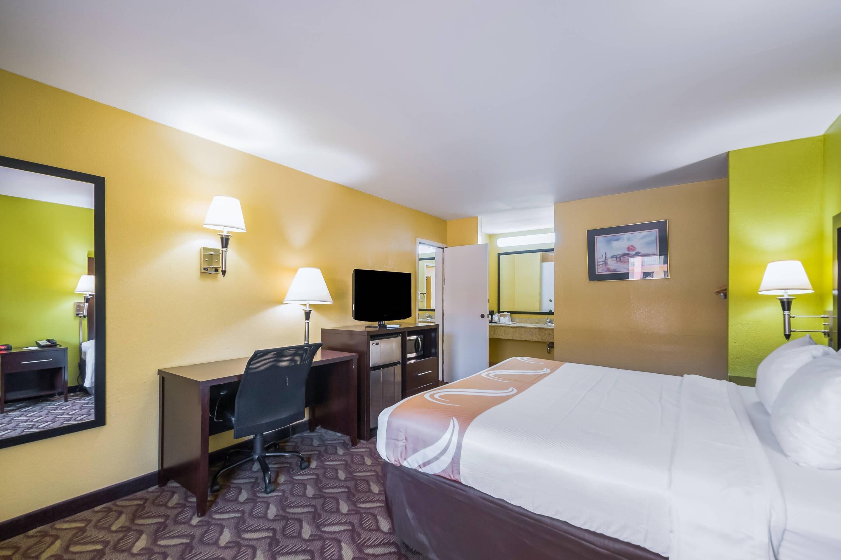 A hotel room with a bed, desk, chair, television, and a mirror.