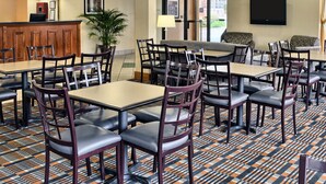 A hotel dining area with multiple tables and chairs, a reception desk, and a large window providing a view of the outside.