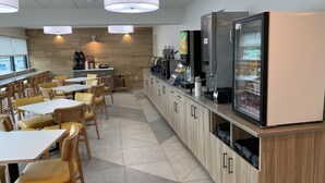 A modern cafe with wooden tables and chairs, a coffee bar, and a refrigerator. - Days Inn & Suites by Wyndham Duluth by the Mall (Duluth)