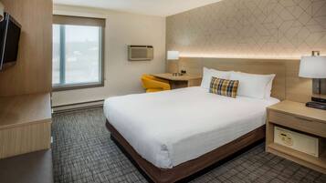 Een hotelkamer met een groot bed, een bureau met stoel, een televisie, een airconditioning en een behangen muur.