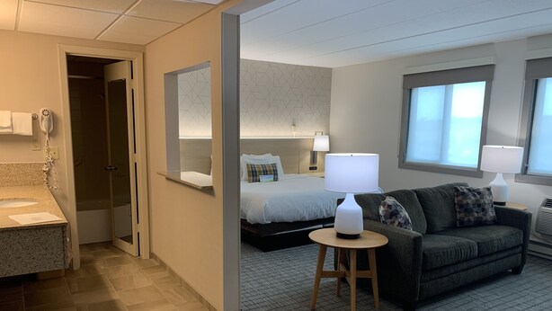 A hotel room with a bathroom, a bed, a sofa, a small table, and a window. - Days Inn & Suites by Wyndham Duluth by the Mall (Duluth)