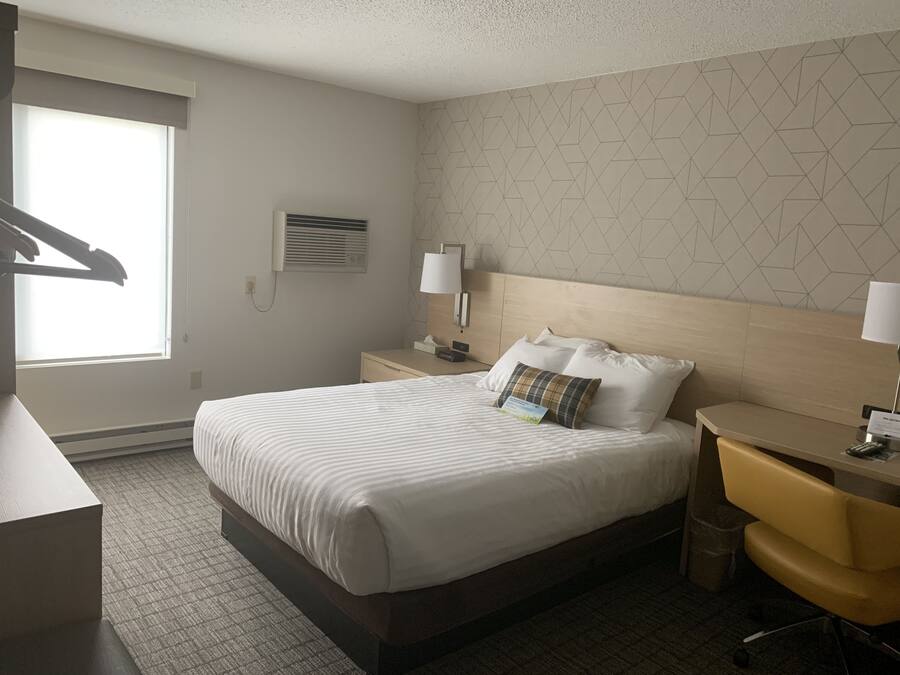 A hotel room with a large bed, a desk, a chair, and a window.