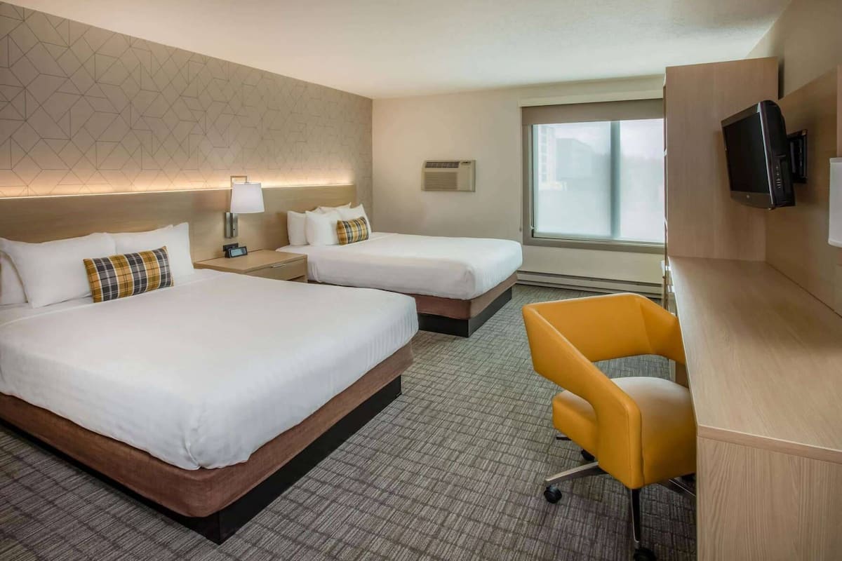 A hotel room with two beds, a desk, a chair, a TV, and a large window.