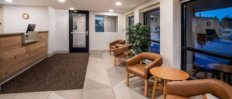 A modern reception area with a wooden desk, a reception counter, and a seating area with leather chairs and a small table.