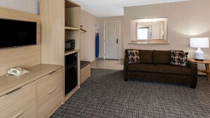 A hotel room with a flat-screen TV, a wooden cabinet, a sofa with patterned cushions, a small table with a lamp, and a mirror on the wall. - Days Inn & Suites by Wyndham Duluth by the Mall (Duluth)