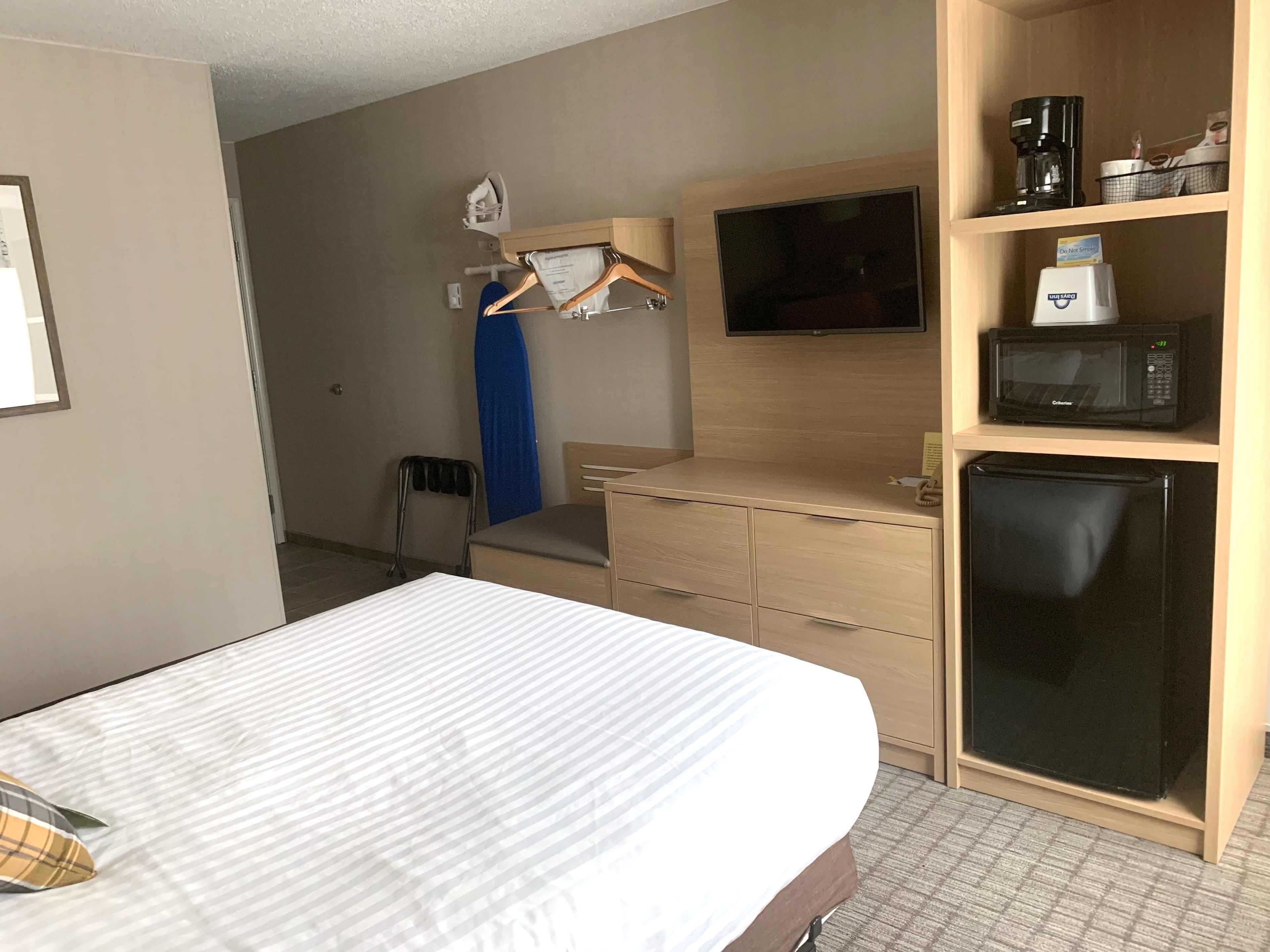 A hotel room with a bed, a desk with a flat-screen TV, a microwave, and a refrigerator.