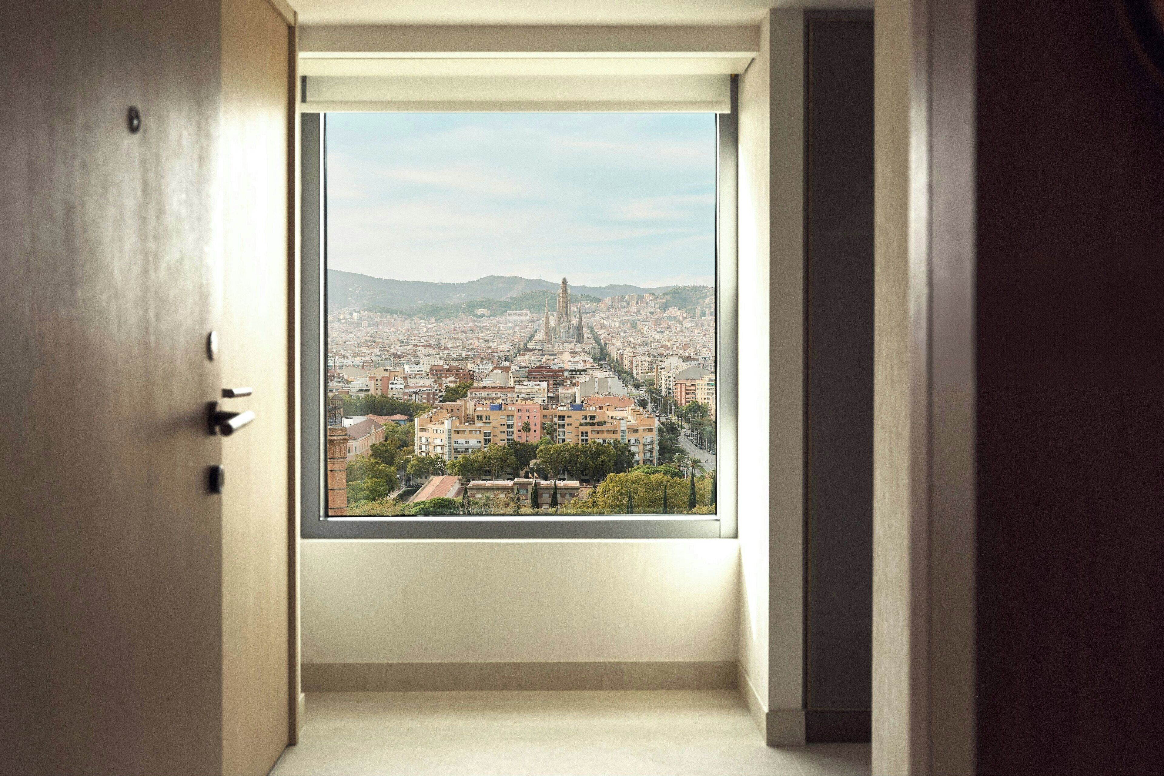 Habitació amb un gran finestral que ofereix vistes a un paisatge urbà, incloent-hi una torre destacada.