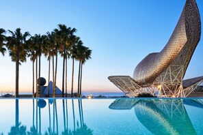 Un área de piscina moderna con una estructura arquitectónica singular, palmeras y una vista despejada del océano.