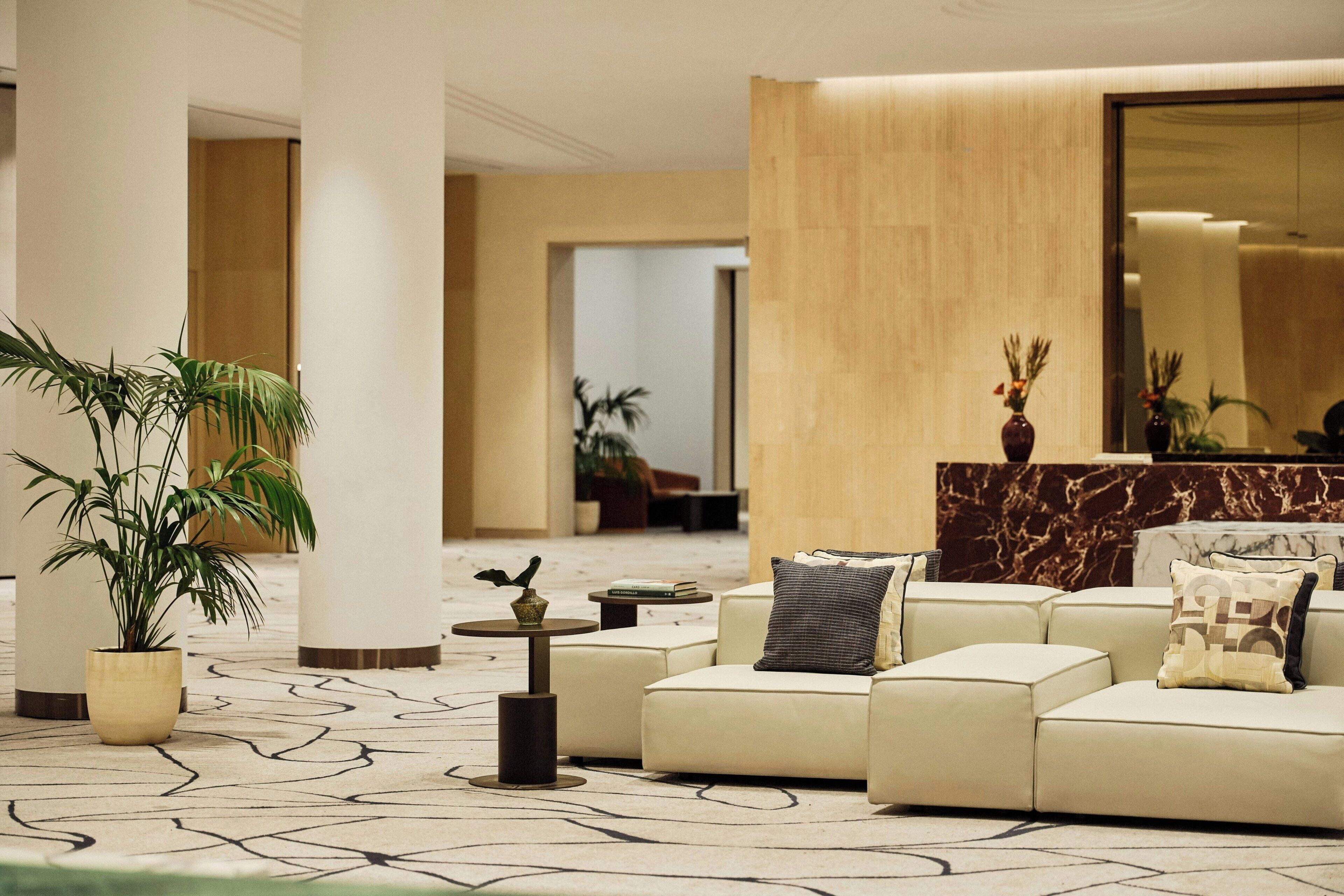 Un moderno vestíbulo con un sofá de color beige, un mostrador de recepción de mármol y un espejo grande.