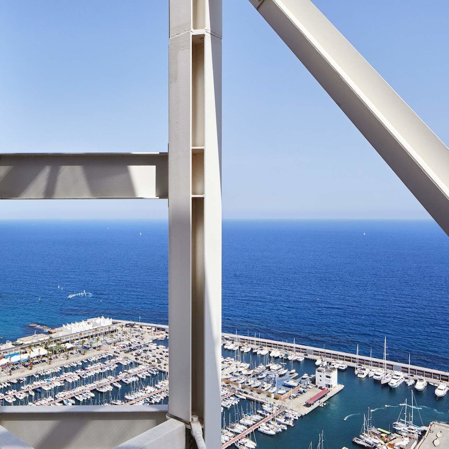 A high vantage point overlooking a marina with boats docked, a beach, and a clear blue sky.