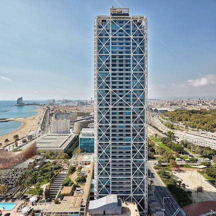 A high-rise hotel with a modern design, located near a beach and cityscape.