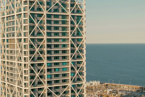 Um edifício alto com fachada em grade e um porto com barcos ao fundo.