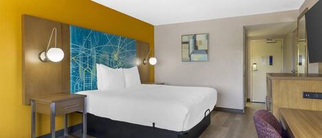 Ett hotellrum med en säng, ett sängbord och ett skrivbord med en stol. Det finns vägglampor och konstverk på väggarna.