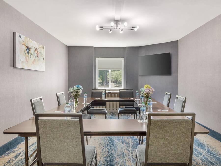 A conference room with a long table, chairs, a large mirror, and a flat-screen TV on the wall.