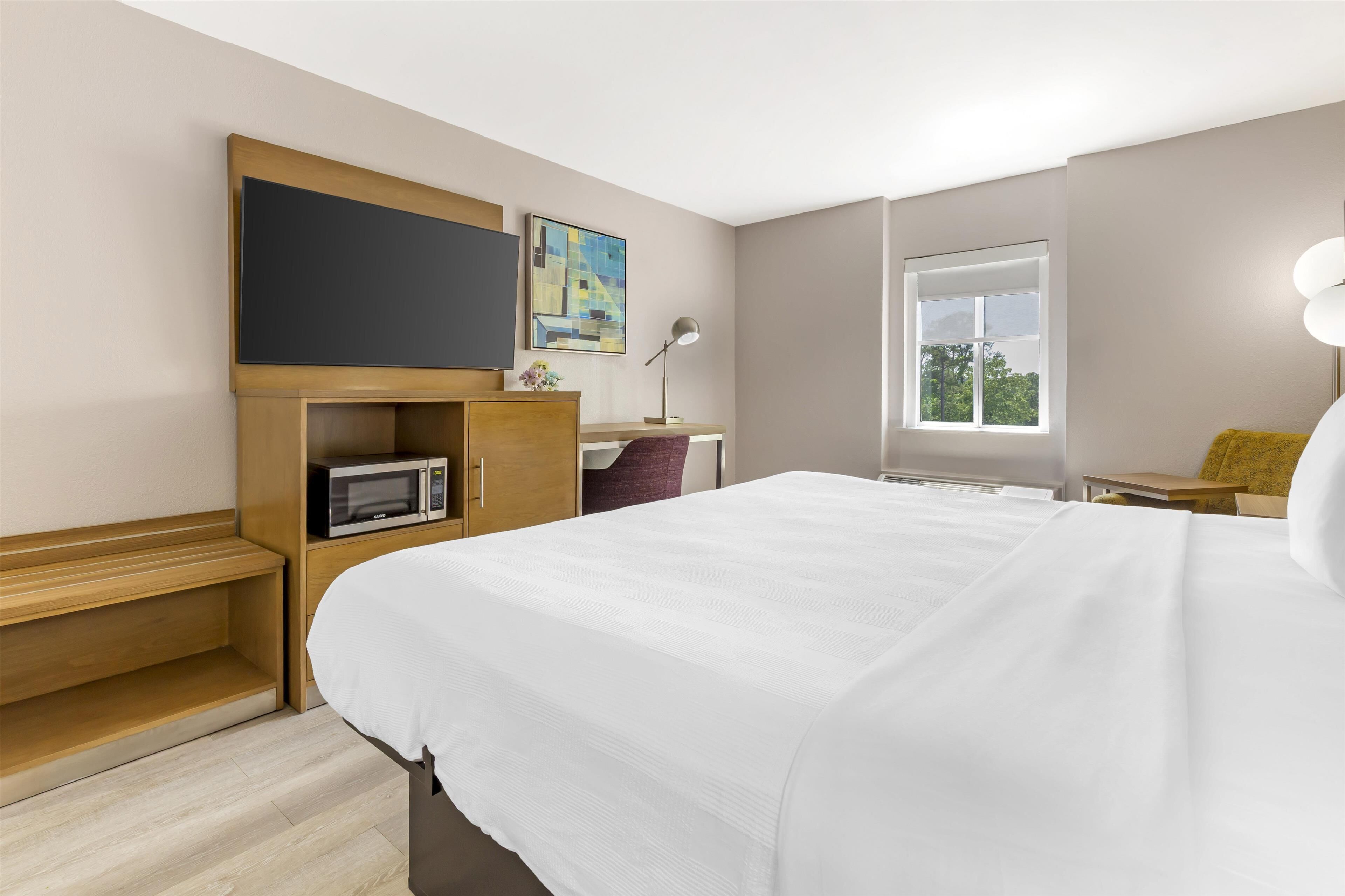 Habitación de hotel con cama, escritorio con computadora, microondas, televisor, ventana y lámpara.