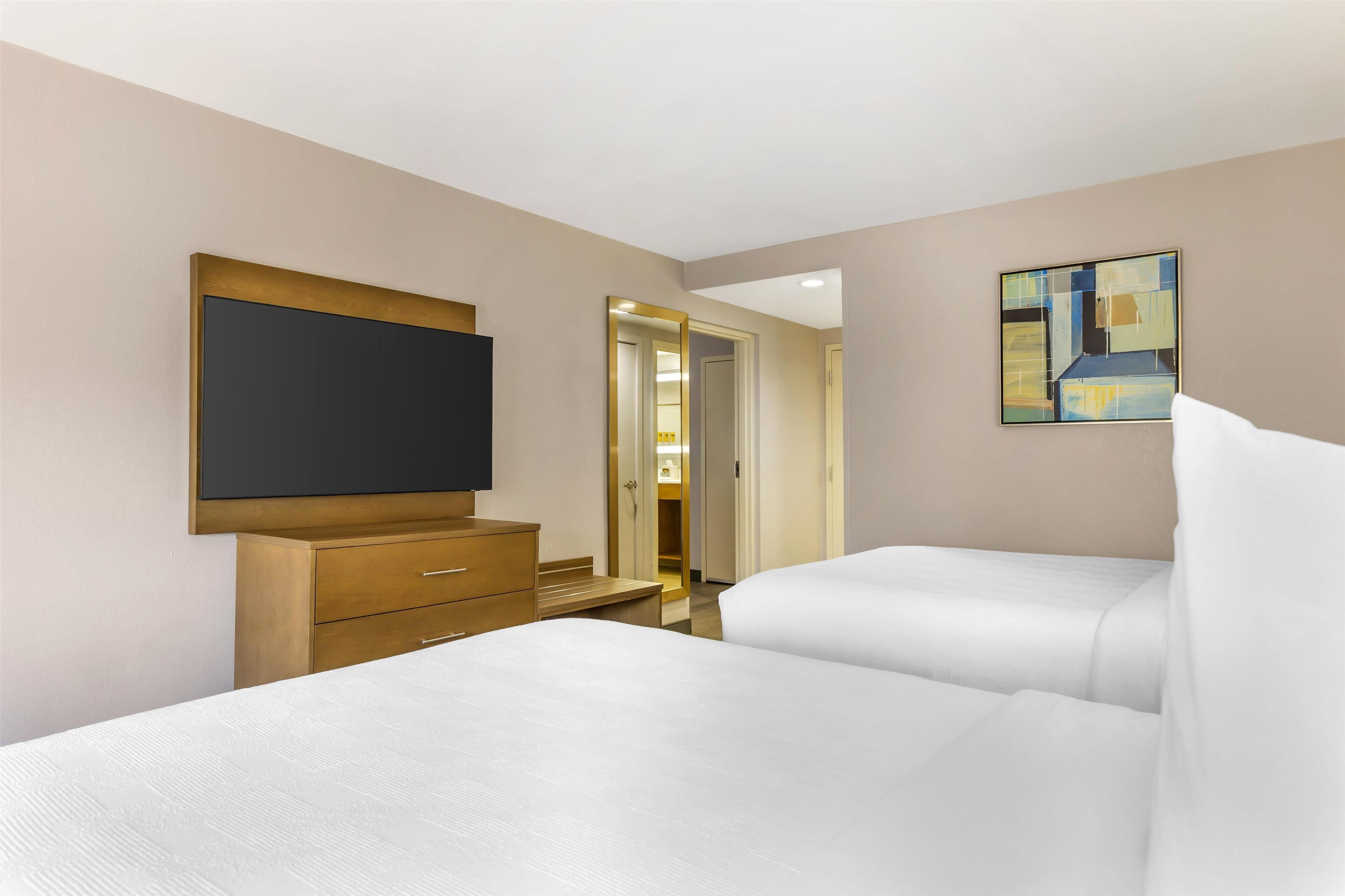 A hotel room with two beds, a TV, a wooden dresser, and a painting on the wall.