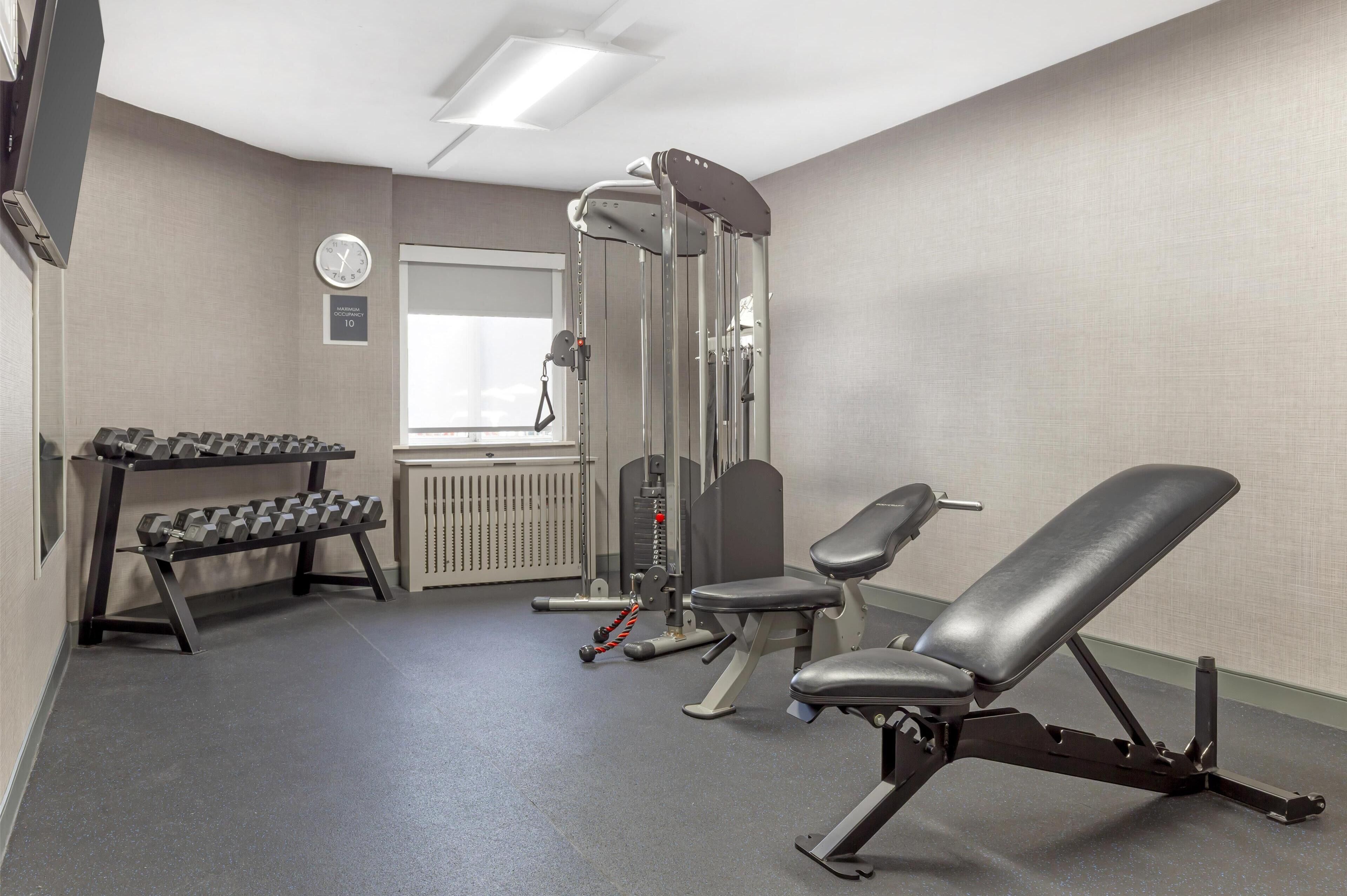 Un gimnasio con una prensa de banca, mancuernas y una máquina de pesas.