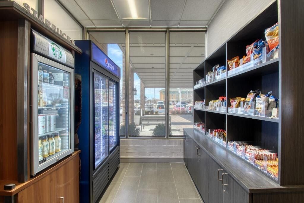 En butiks indretning med køledisplaye, reoler fyldt med snacks, og udsigt gennem glasdøren.