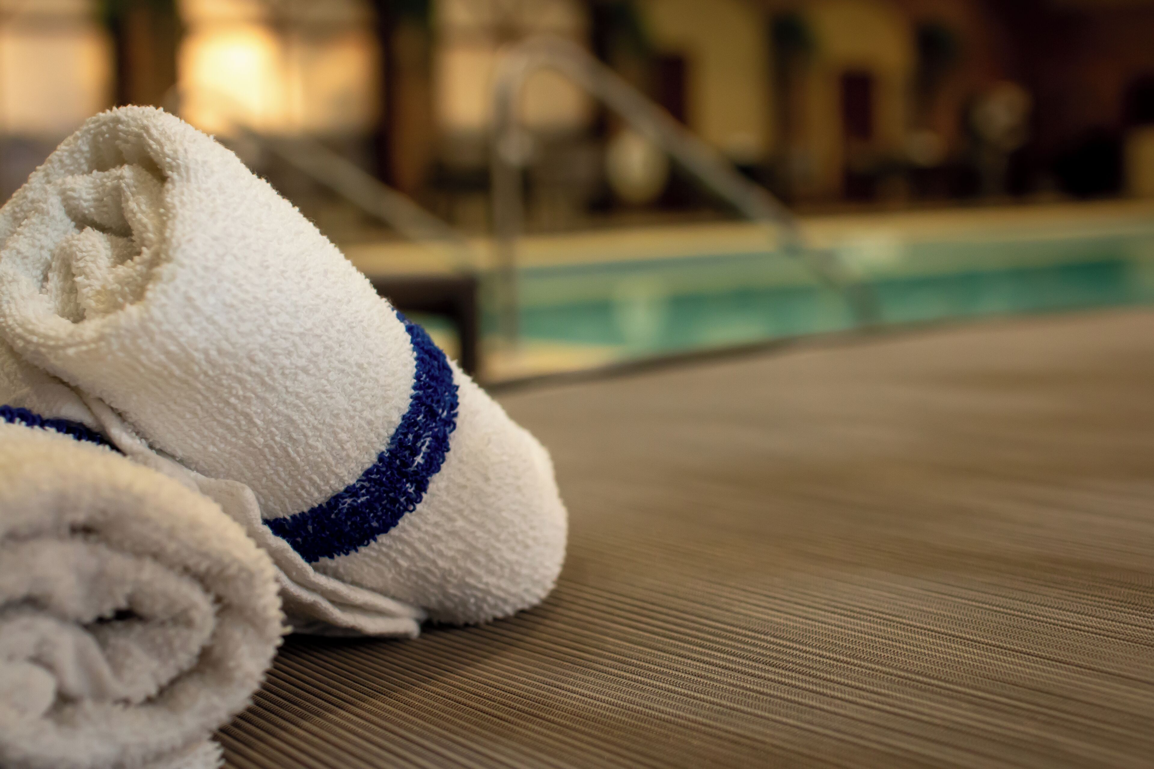 A pair of rolled towels with a blue stripe on a textured surface, likely a poolside area.