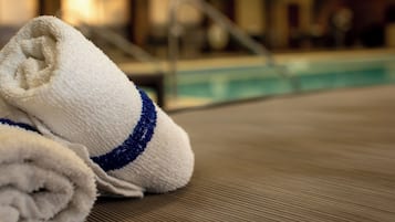 Un par de toallas enrolladas con un listón azul sobre una superficie texturizada, probablemente en una zona junto a la piscina.
