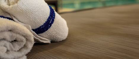 A pair of rolled towels with a blue stripe on a textured surface, likely a poolside area.