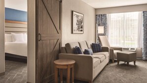 A hotel room with a bed, a sofa, a chair, a small table, and a large window with curtains. - Radisson Hotel and Conference Center Fond du Lac (Fond du Lac)