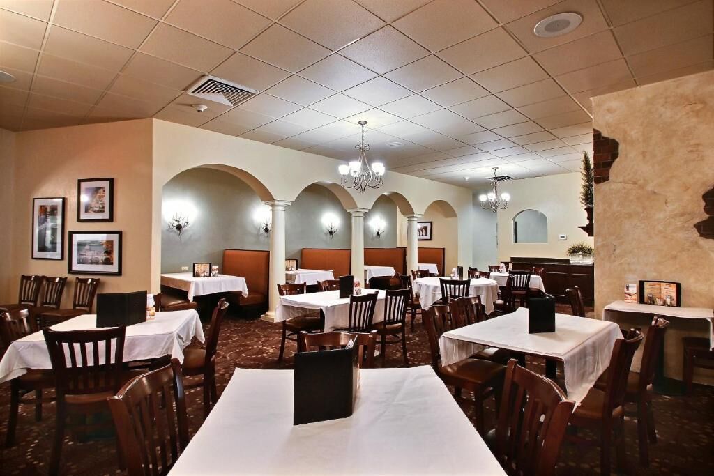 A restaurant with multiple tables and booths, white tablecloths, and wooden chairs.