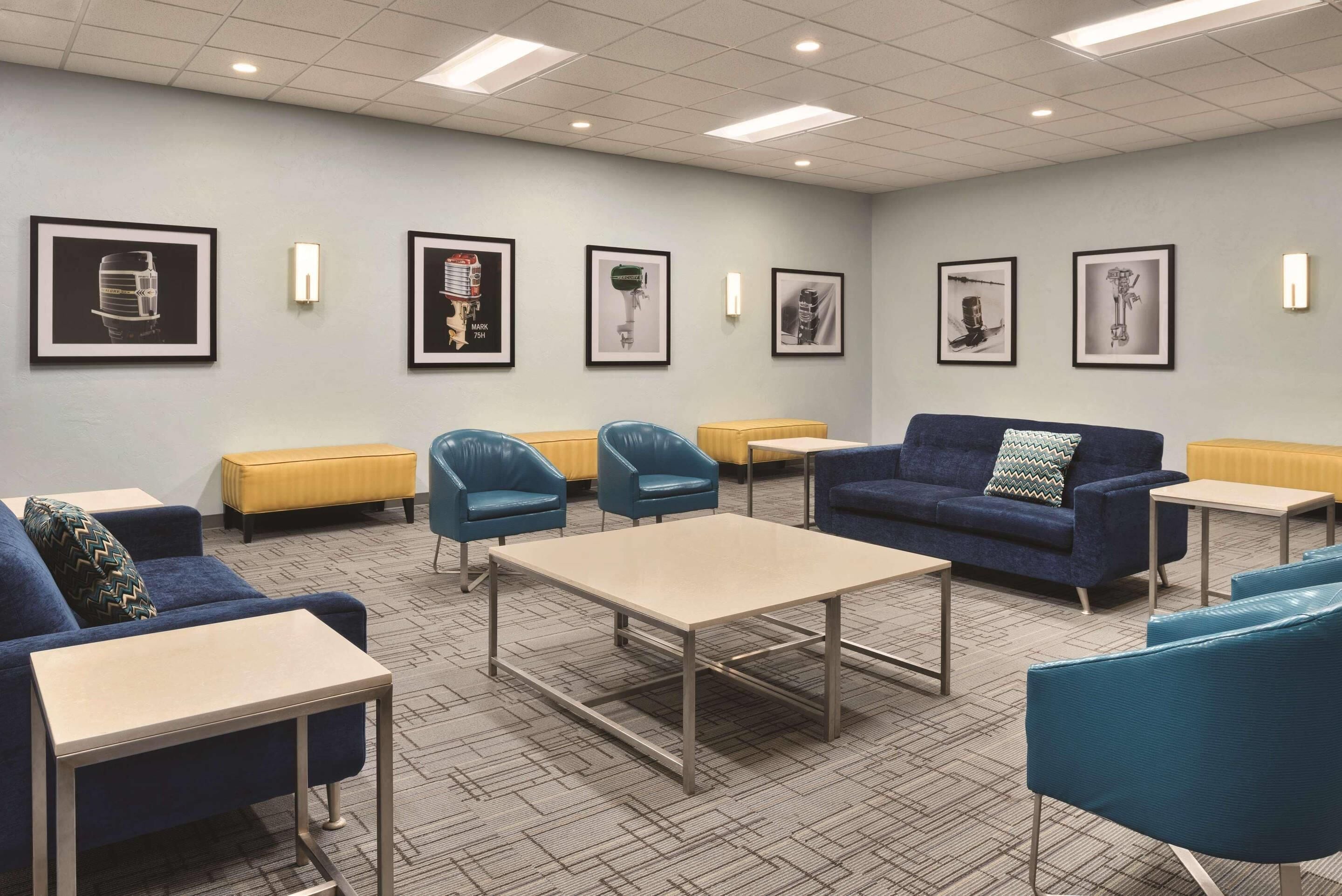 A modern lounge area with blue sofas, armchairs, and a central table, featuring framed artwork on the walls.