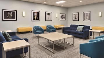 A modern lounge area with blue sofas, armchairs, and a central table, featuring framed artwork on the walls.