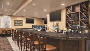 A bar area with a long counter, multiple bar stools, a wine rack, and a television screen. - Radisson Hotel and Conference Center Fond du Lac (Fond du Lac)
