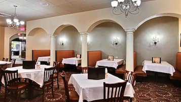 Un restaurante con mesas y sillas, candelabros y una alfombra estampada.